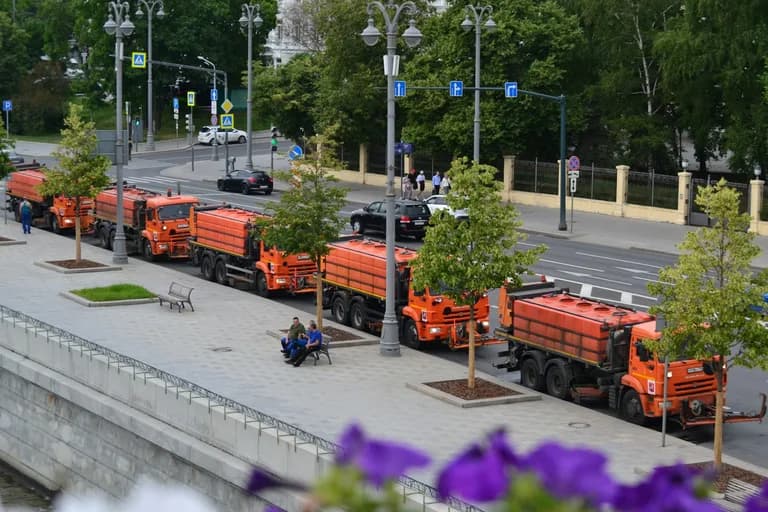 Ağaçlı bir kent caddesinde sıra hâlinde park etmiş turuncu temizlik araçları